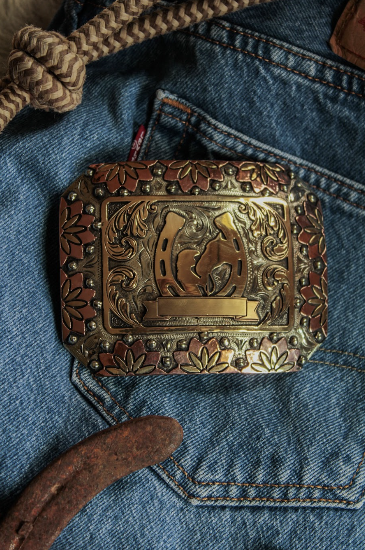 Copper and brass horseshoe trophy buckle with a blank nameplate laid on a denim jacket
