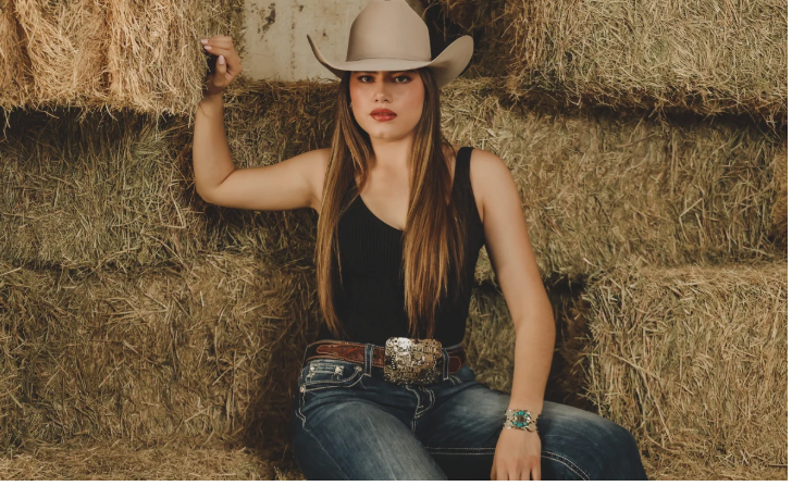 Woman on hay bales in a cowboy hat wearing a Supreme belt buckle