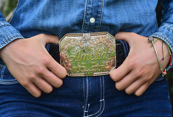Hand-engraved green and gold name buckle worn on a denim shirt and jeans